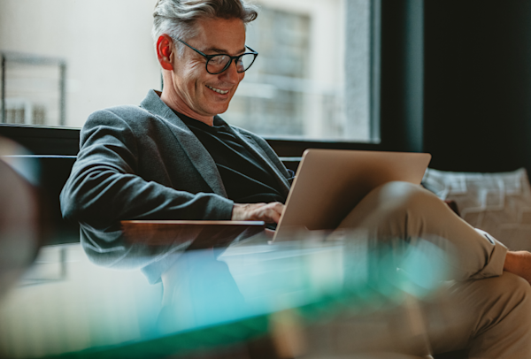 Smiling businessman sitting in office lobby working on laptop