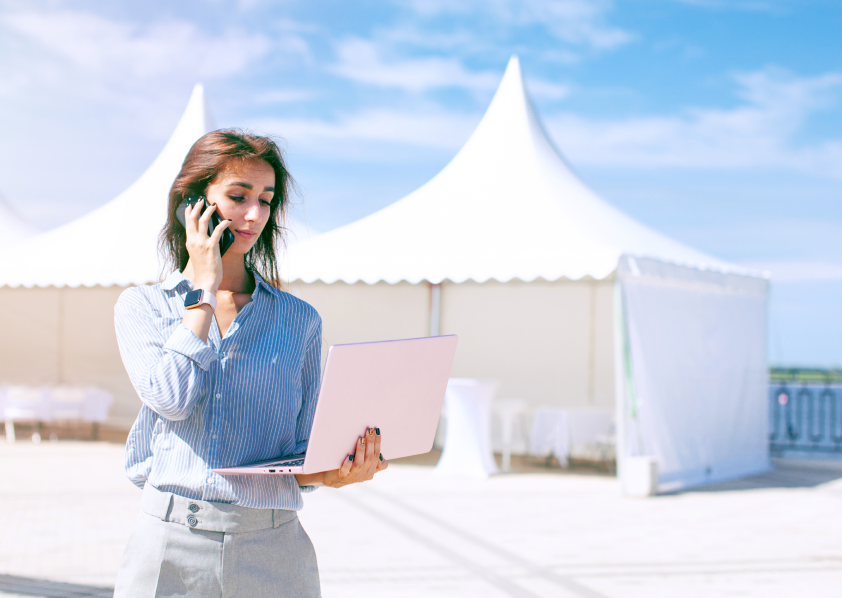 Woman on the phone and her laptop with event tents in the background