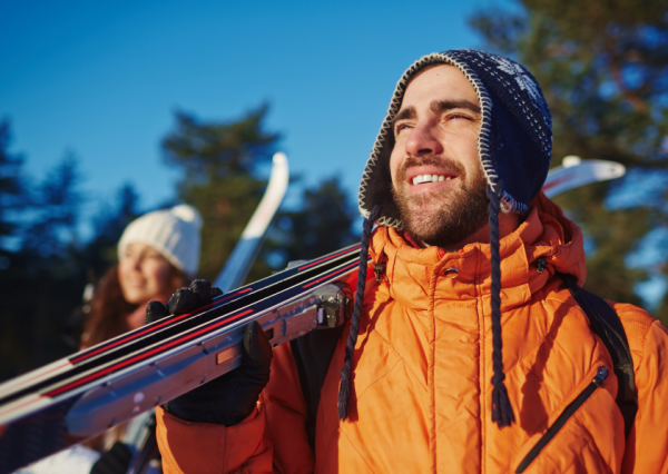 Smiling man holding skis with woman looking in the background
