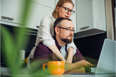 Man is sitting with woman standing above him with arms resting on his shoulders