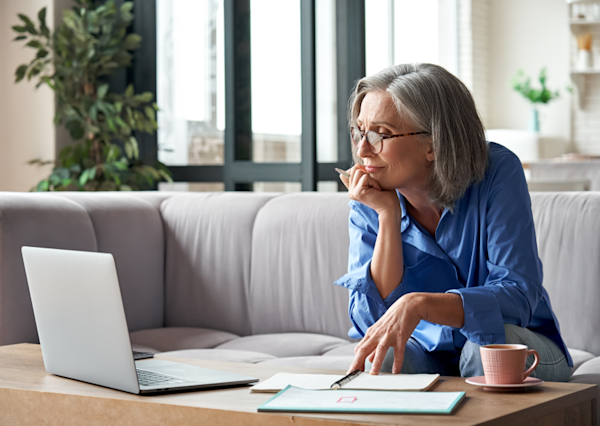 A mature woman looking at her laptop with her hand on a notepad