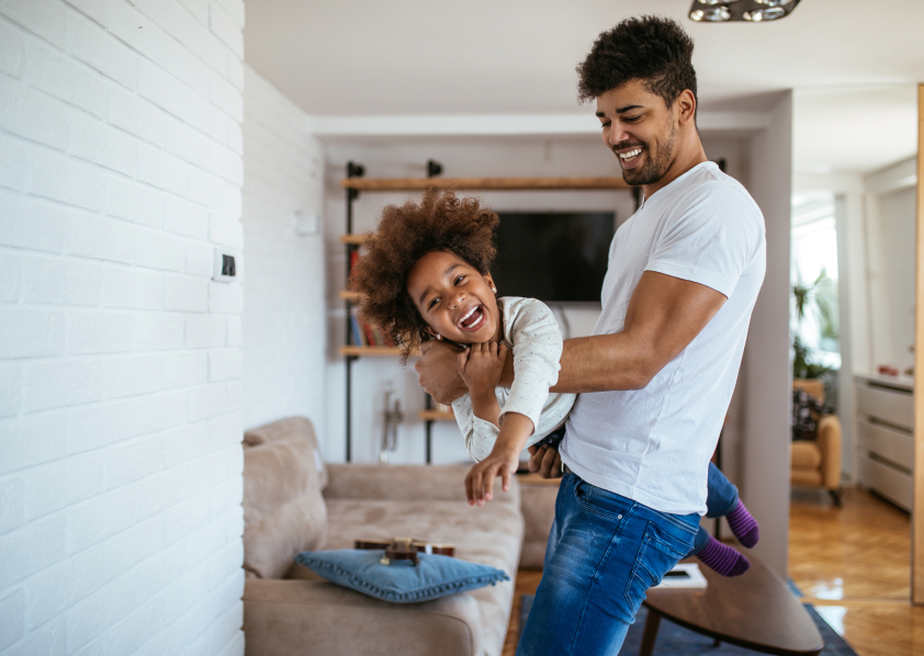 Young man spinning his daughter around in living room