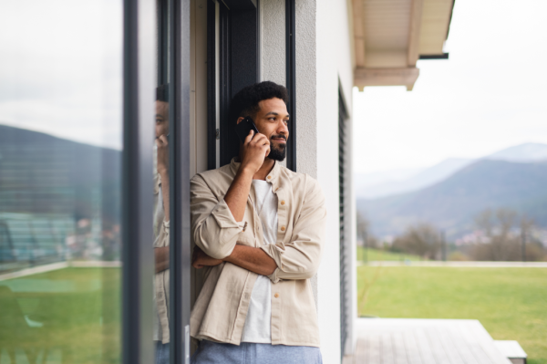 Man standing in a doorway, looking outside while on his cellphone