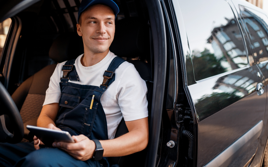 A courier looking off in the distance, holding a tablet and sitting in his van