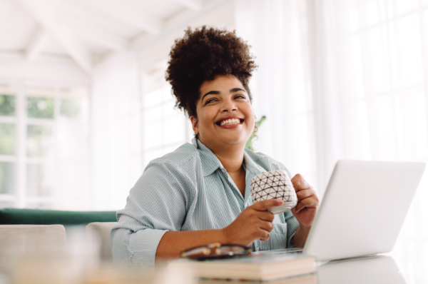 Wide angle shot of woman sitting on table with coffee mug and laptop