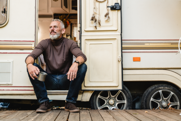 Mature man sitting in the doorway of an RV, looking outside with a mug in hand