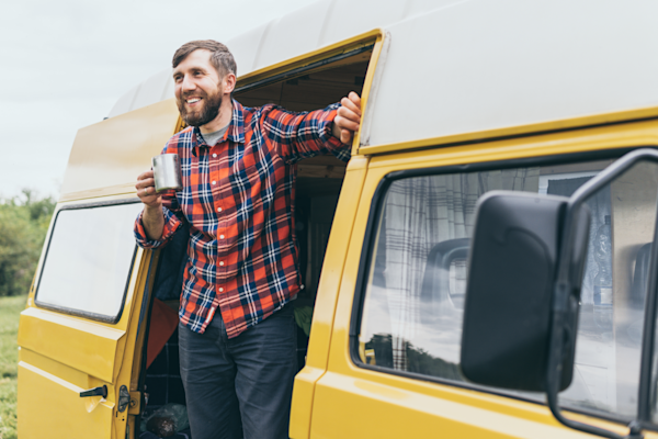 Man standing in the doorway of a yellow and white van, looking outside and holding a mug