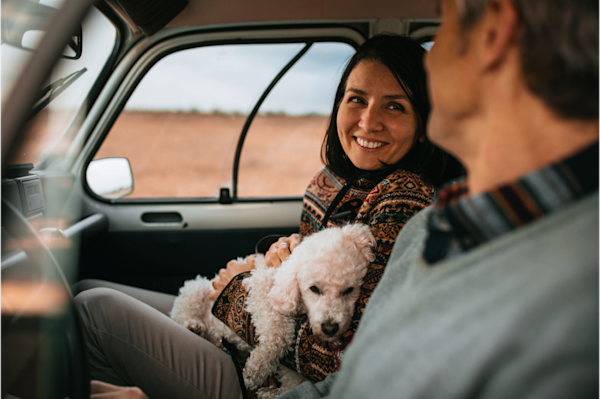 Woman holding a dog on her lap in the passenger seat with a man looking at her in the driver's seat