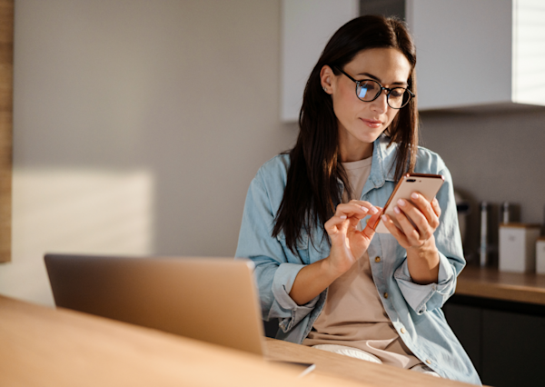 Woman at home using her phone while on her laptop