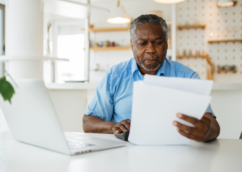 Mature man sitting at home on his laptop, looking at paperwork