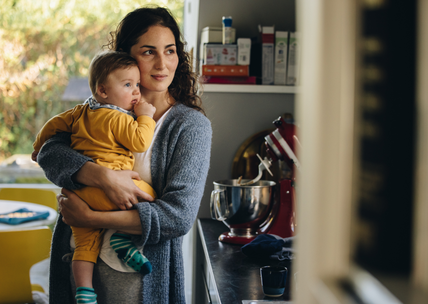 Woman holding baby in the kitchen and looking off in the distance