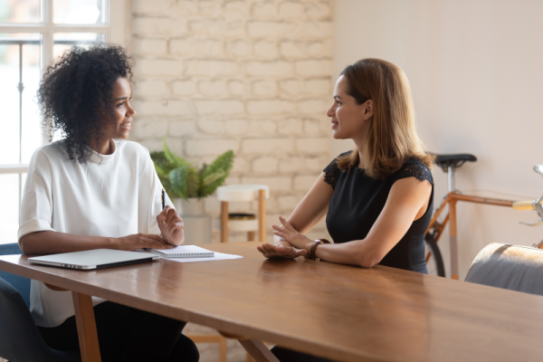 Smiling young businesswoman talking with female job candidate at office meeting