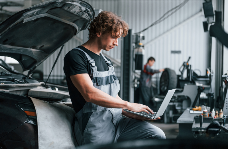 Mechanic leaning on vehicle on a laptop