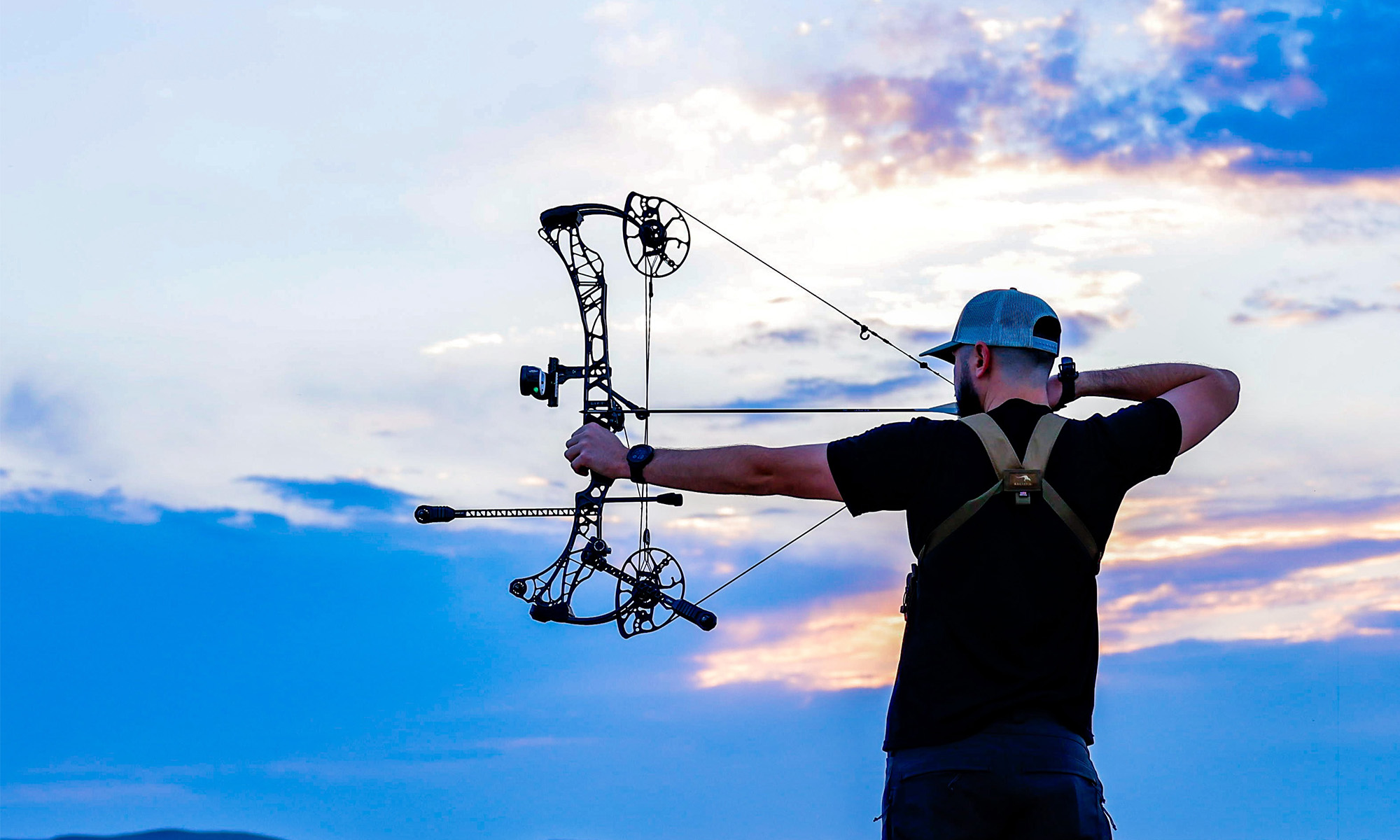 A hunter shoots a bow with sky in the background. 