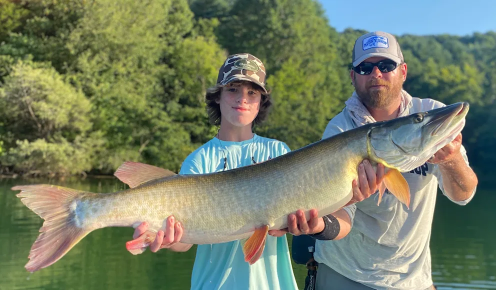 A pair of anglers hold up a big muskie caught from a lake.