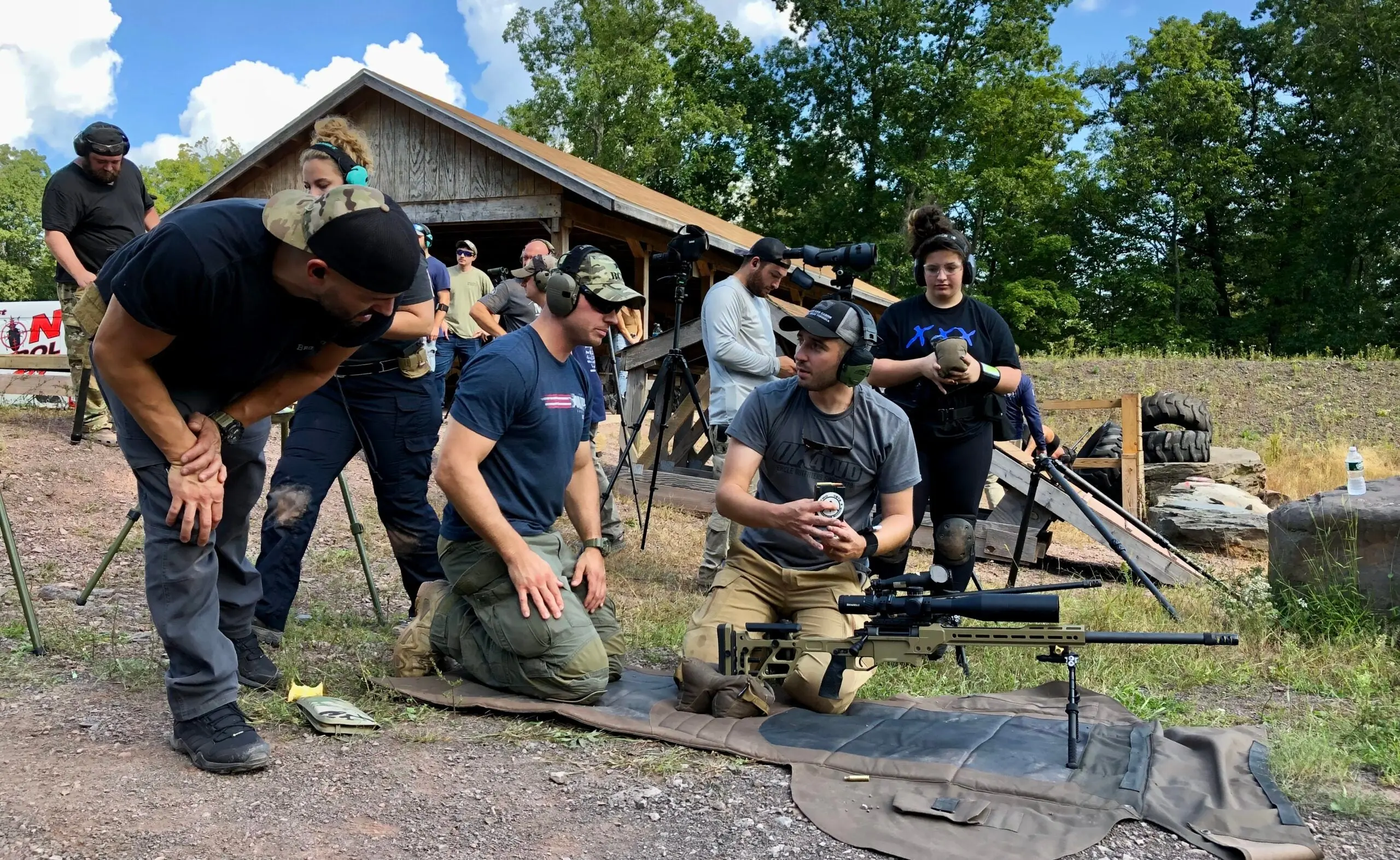 A shooter kneels behind his rifle and confers with other shooters at a PRS match.