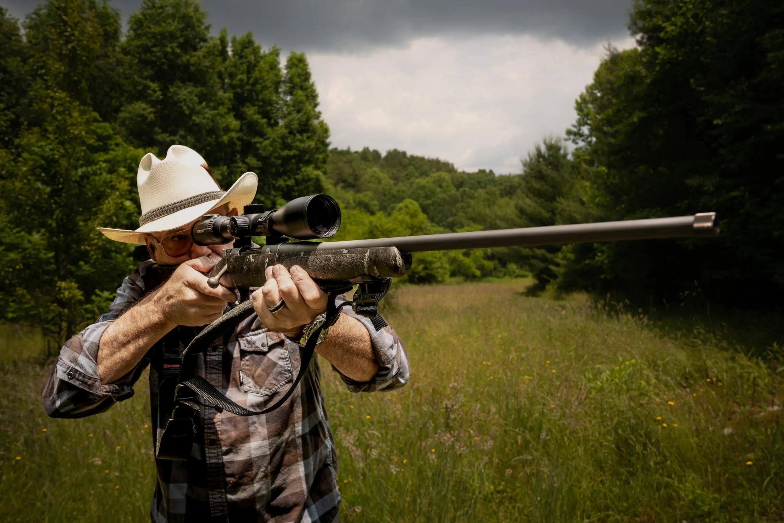 Man standing in green field shooting a rifle from the offhand position