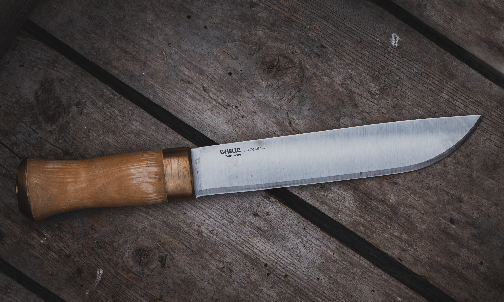 A Helle Lappland, one of the best camp knives ever made, lies on wooden planks. 