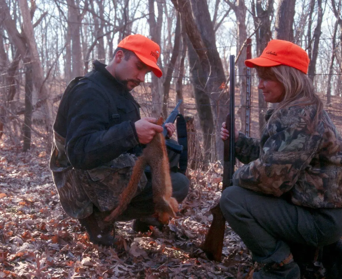 Two hunters hold up squirrels in the woods.