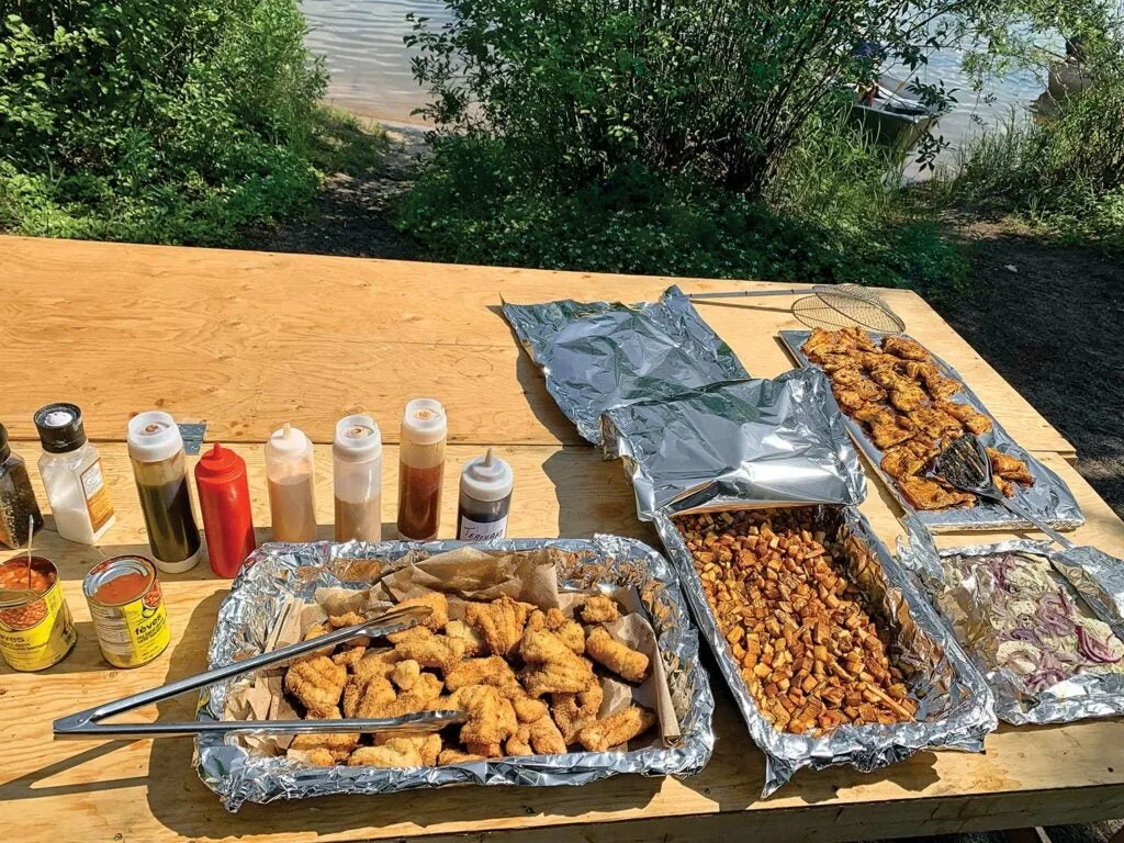 A long table filled with pans of fried  fish, beans, and other food items next to bottles of condiments.