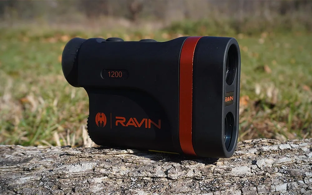 A black and orange Ravin 1200 rangefinder sitting on a grey log in a lawn.