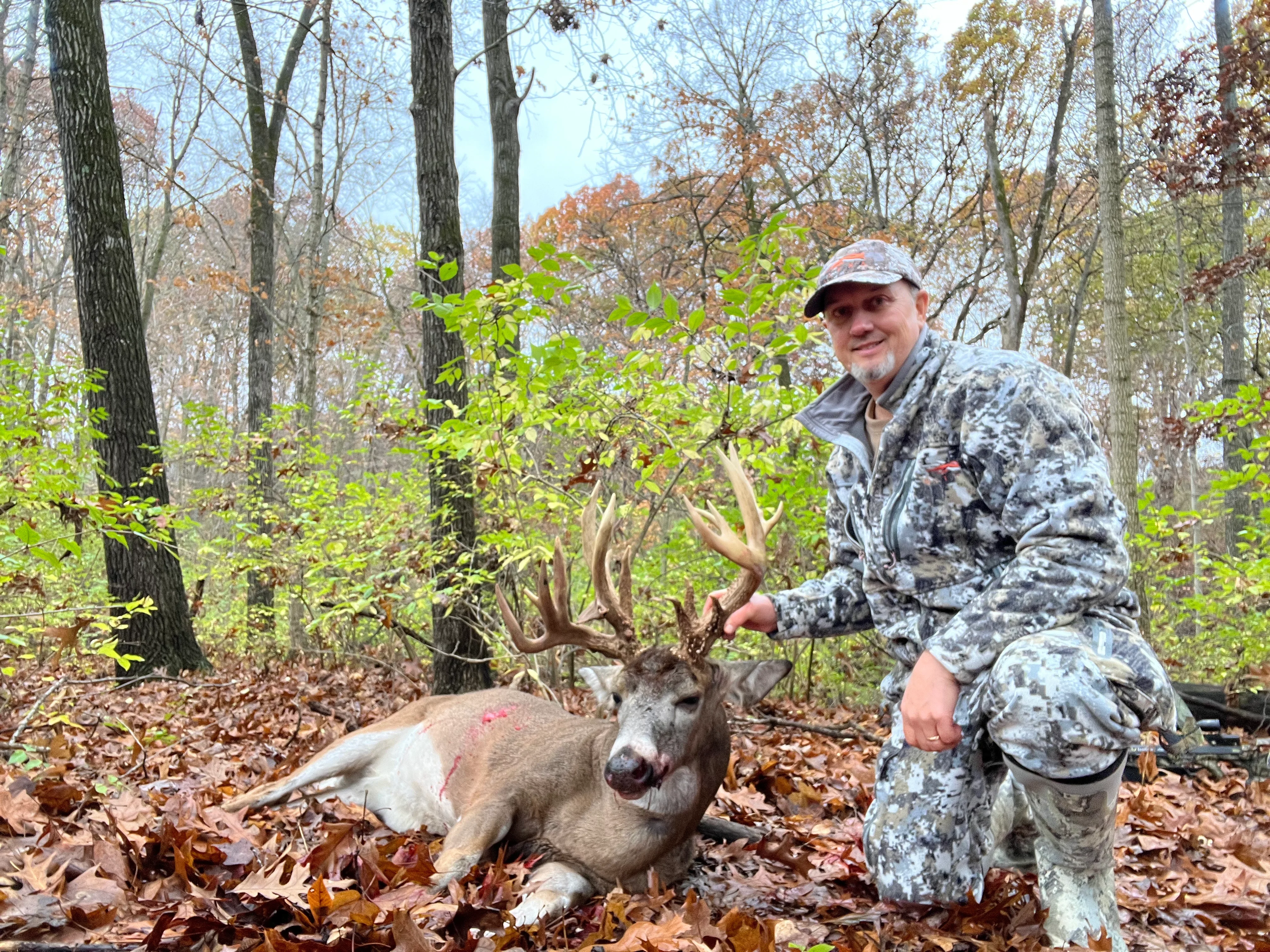 An Illinois hunter poses in the woods with a trophy whitetail buck. 