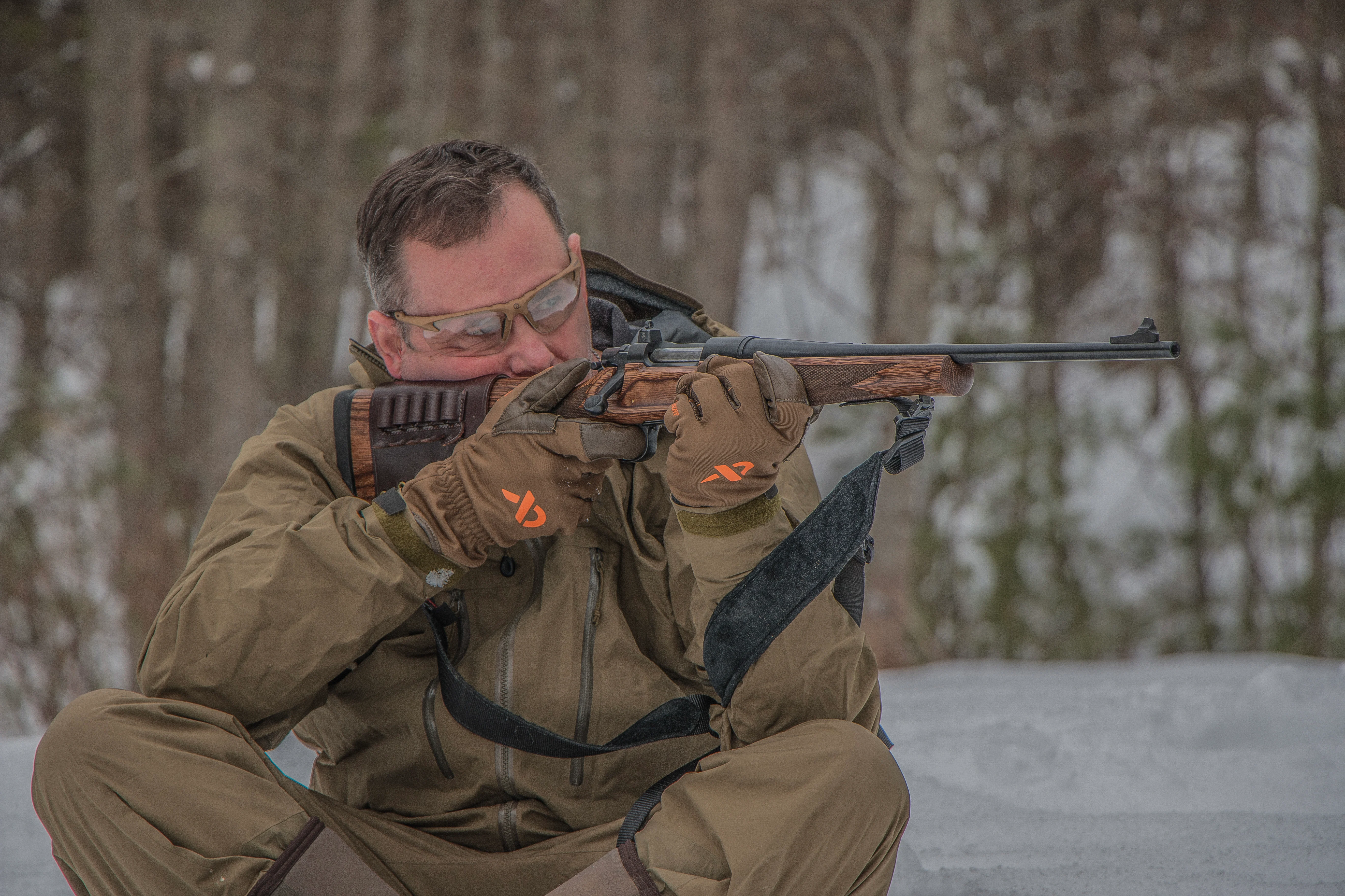 A shooter fires a rifle from the seated position while using a shooting sling for support. 