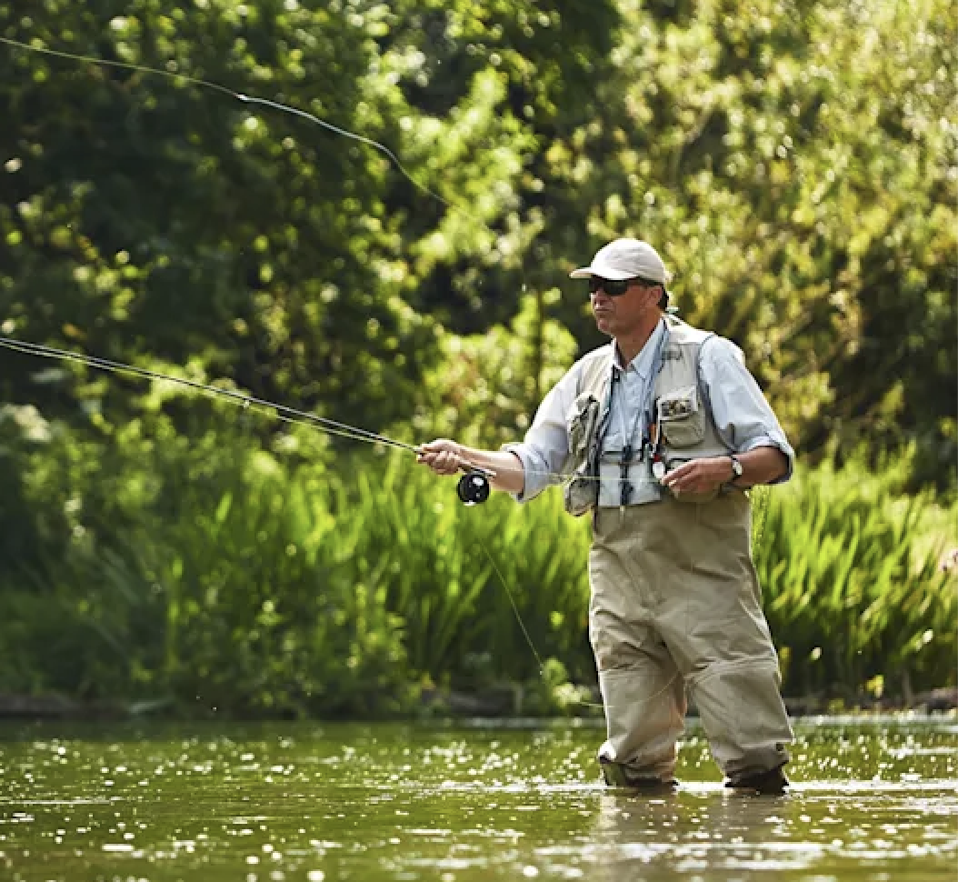 A man fly fishing in a river in summer.