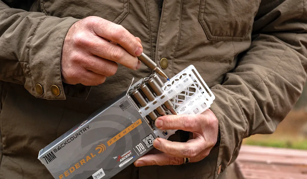A shooter pulls a cartridge from a box of rifle ammo.