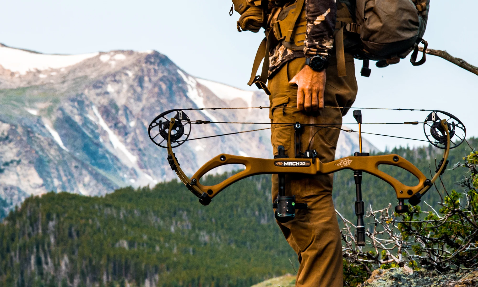 A hunter holding the new PSE Mach 33 DS compound bow with mountains in background. 