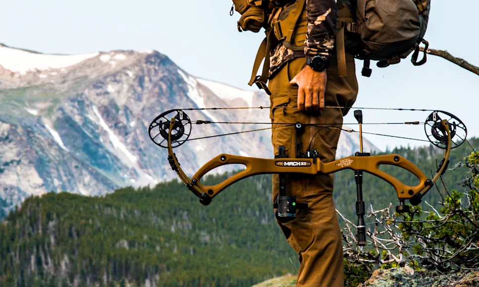 A hunter holding the new PSE Mach 33 DS compound bow with mountains in background.