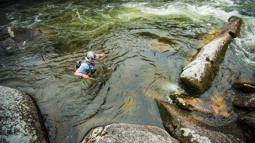 angler wades through chest-high water in rocky river