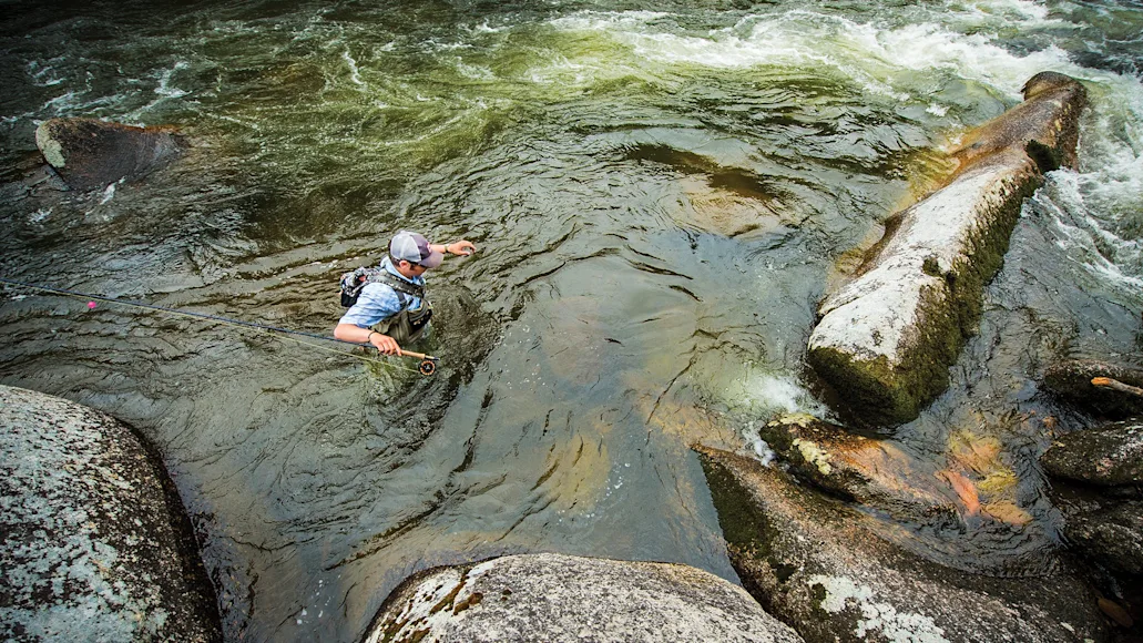 angler wades through chest-high water in rocky river
