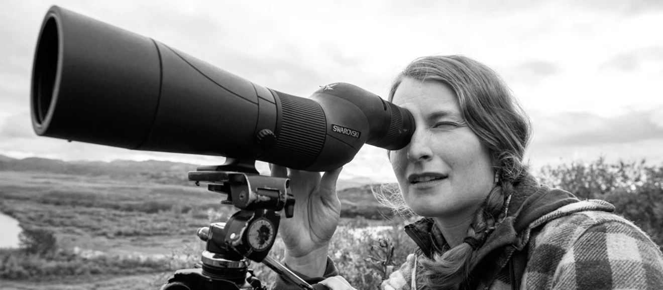 Alaska bear guide Tia Shoemaker looks through a Swarovski spotting scope along a river. 