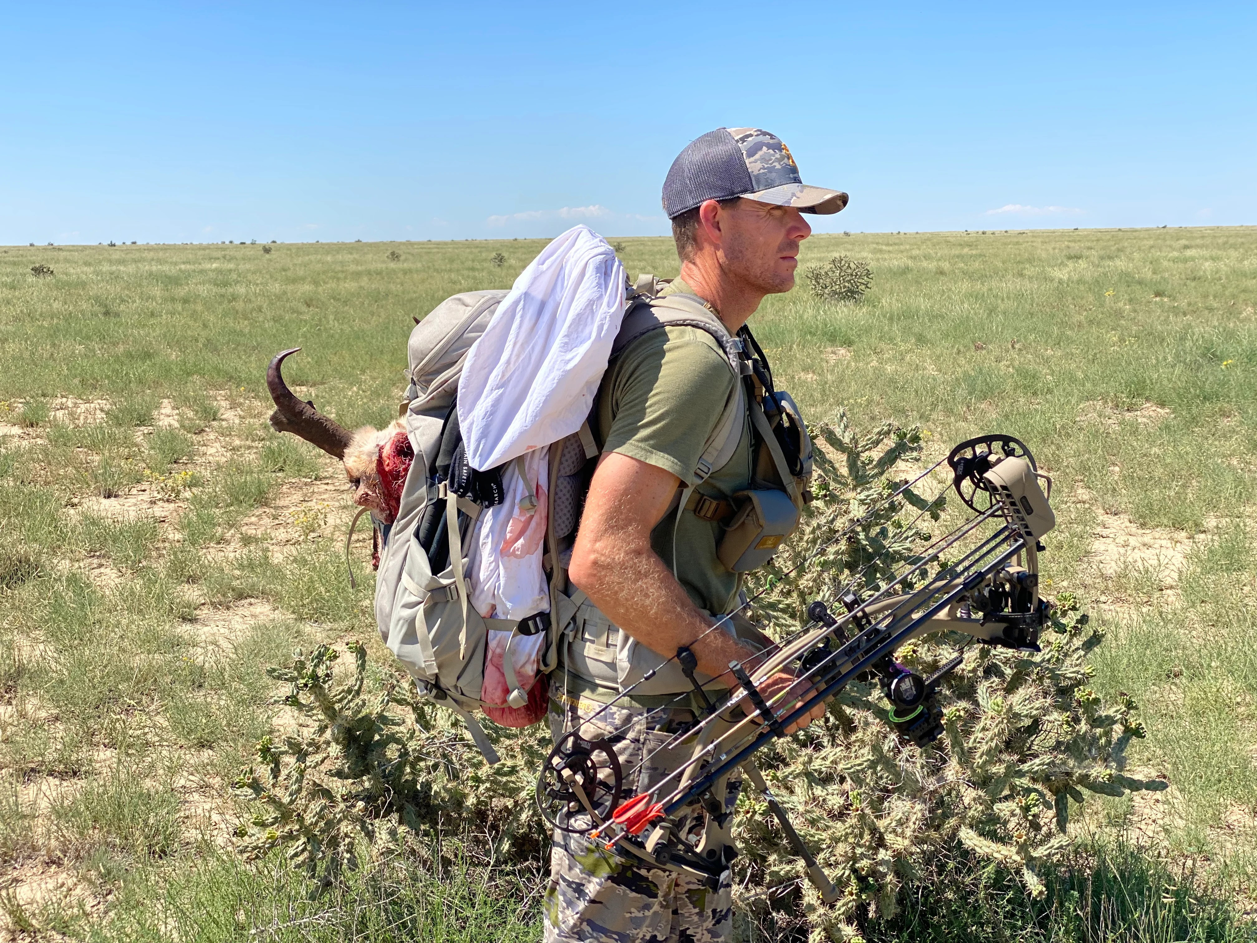 Bowhunter packing out a pronghorn buck across open plains