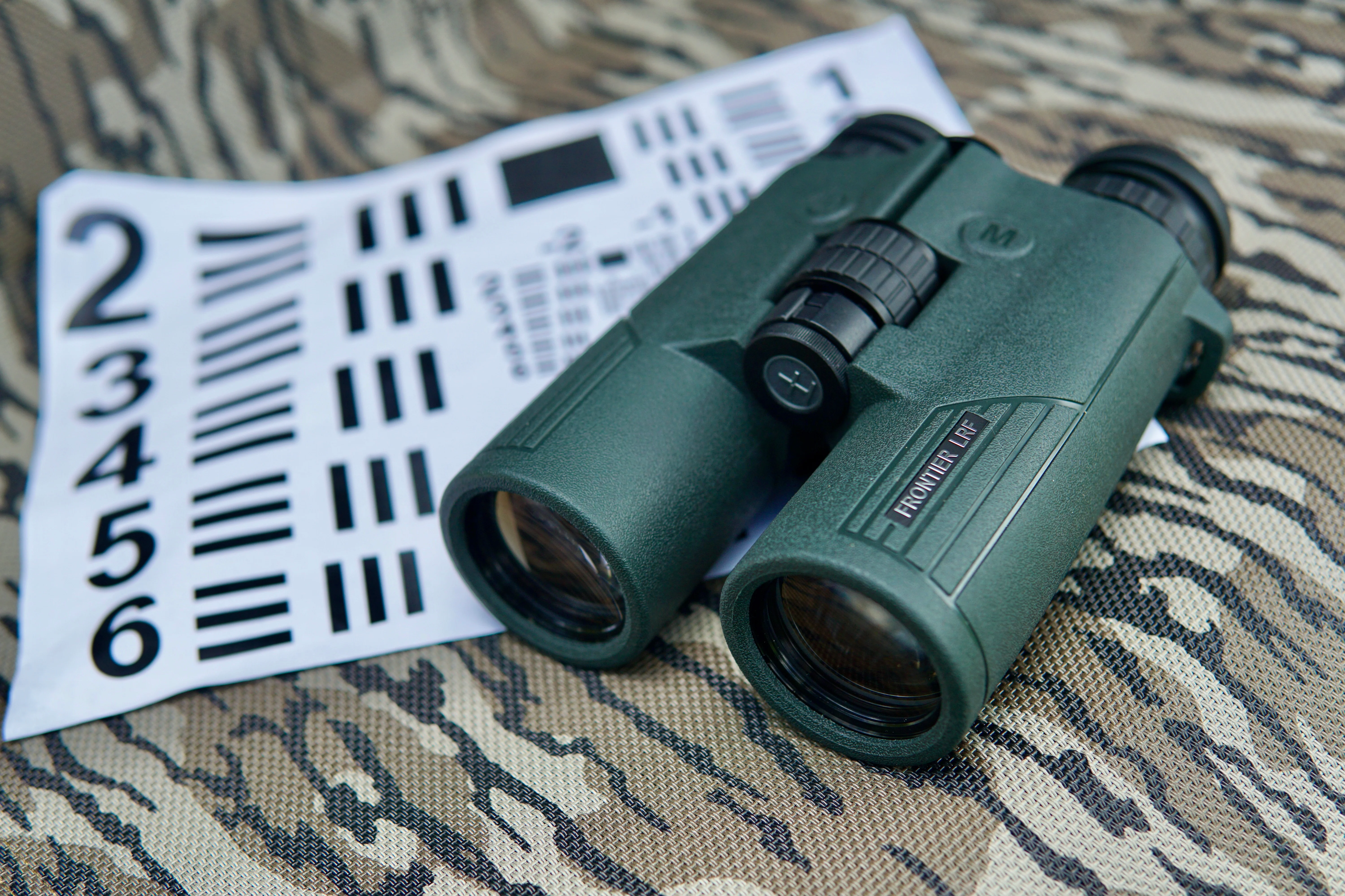 Hawke Frontier LRF binoculars resting on camo fabric next to a resolution chart. 