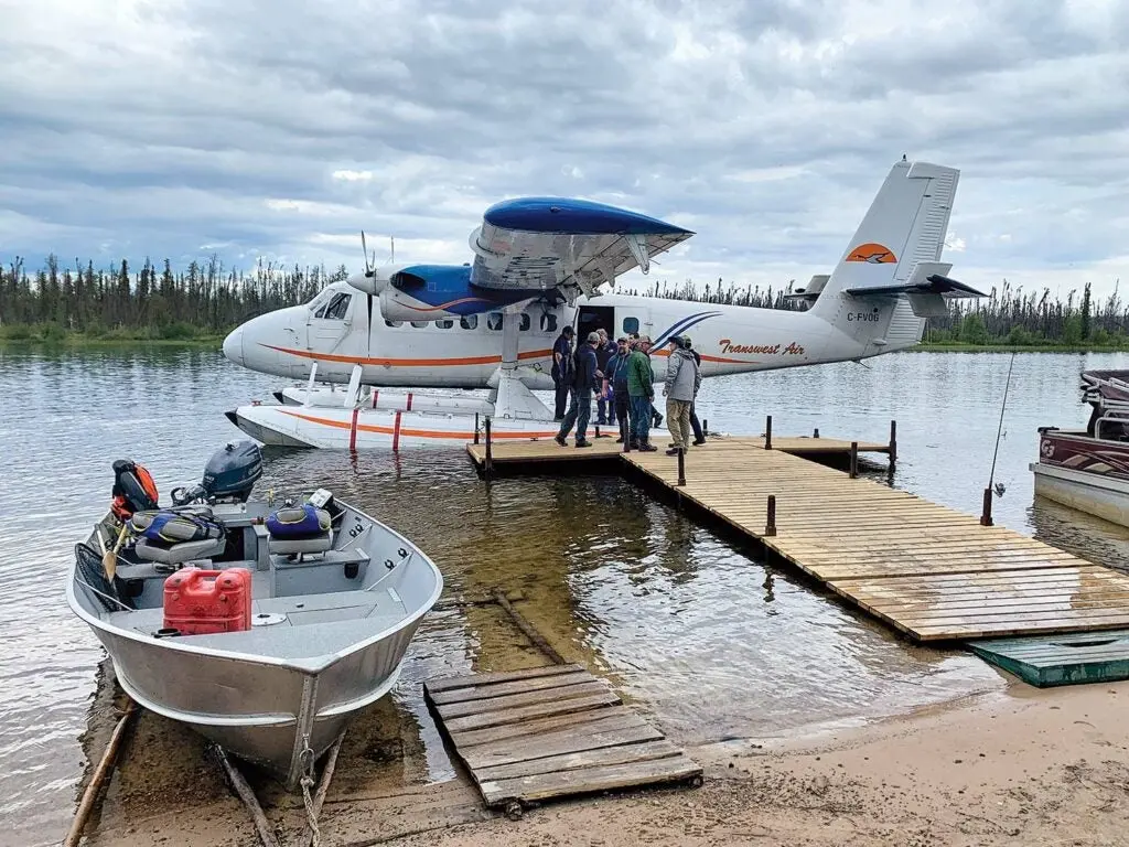 A large floatplane at the docks of a fishing camp next to an aluminum outboard boat.