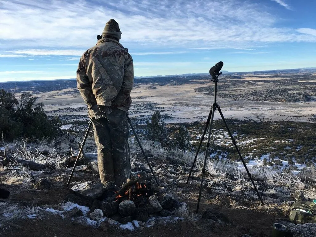 Hunter scouting a large countryside with a spotting scope.