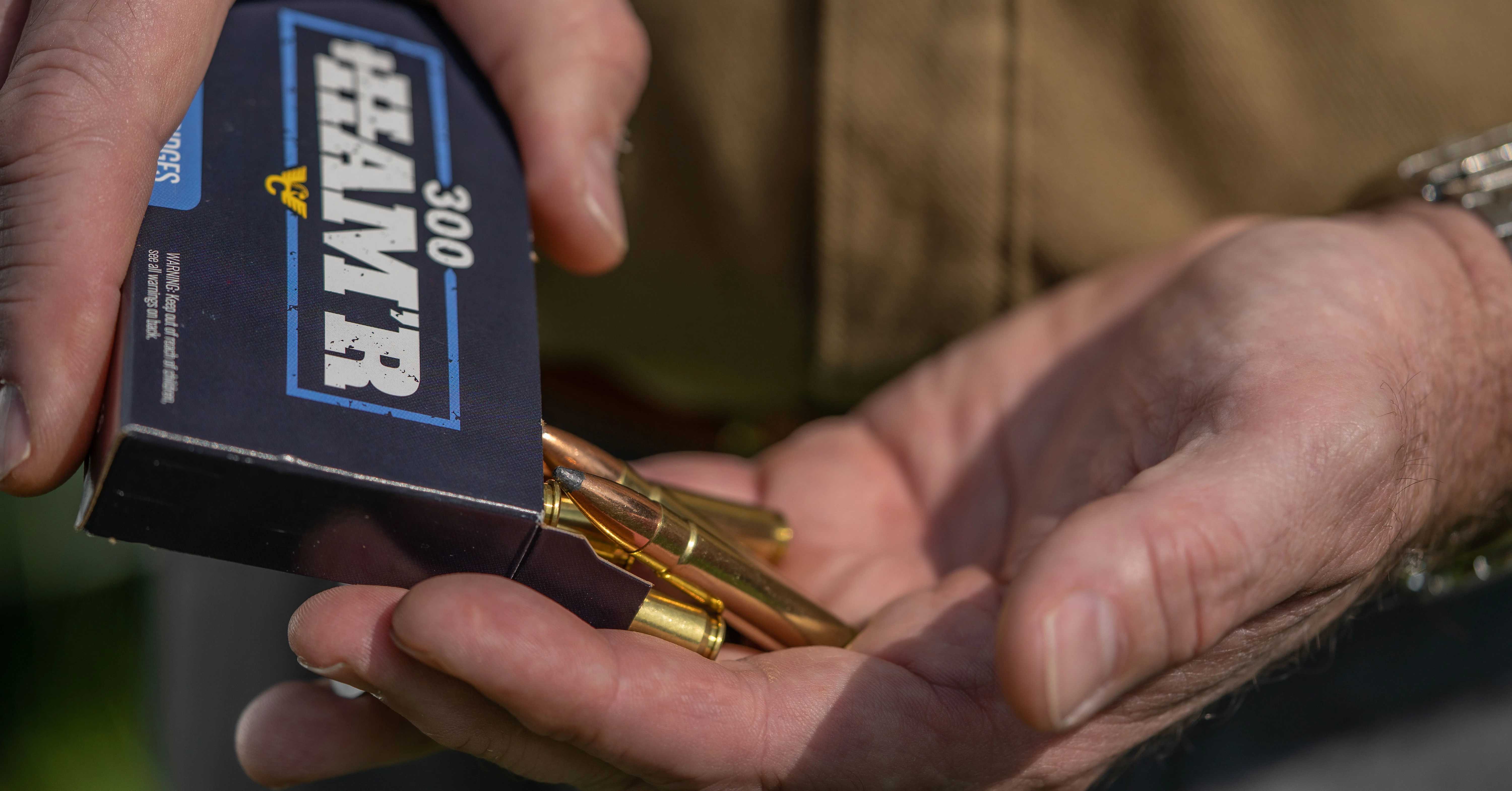A shooter takes a handful of rifle cartridges from a box of 300 HAMR ammo.