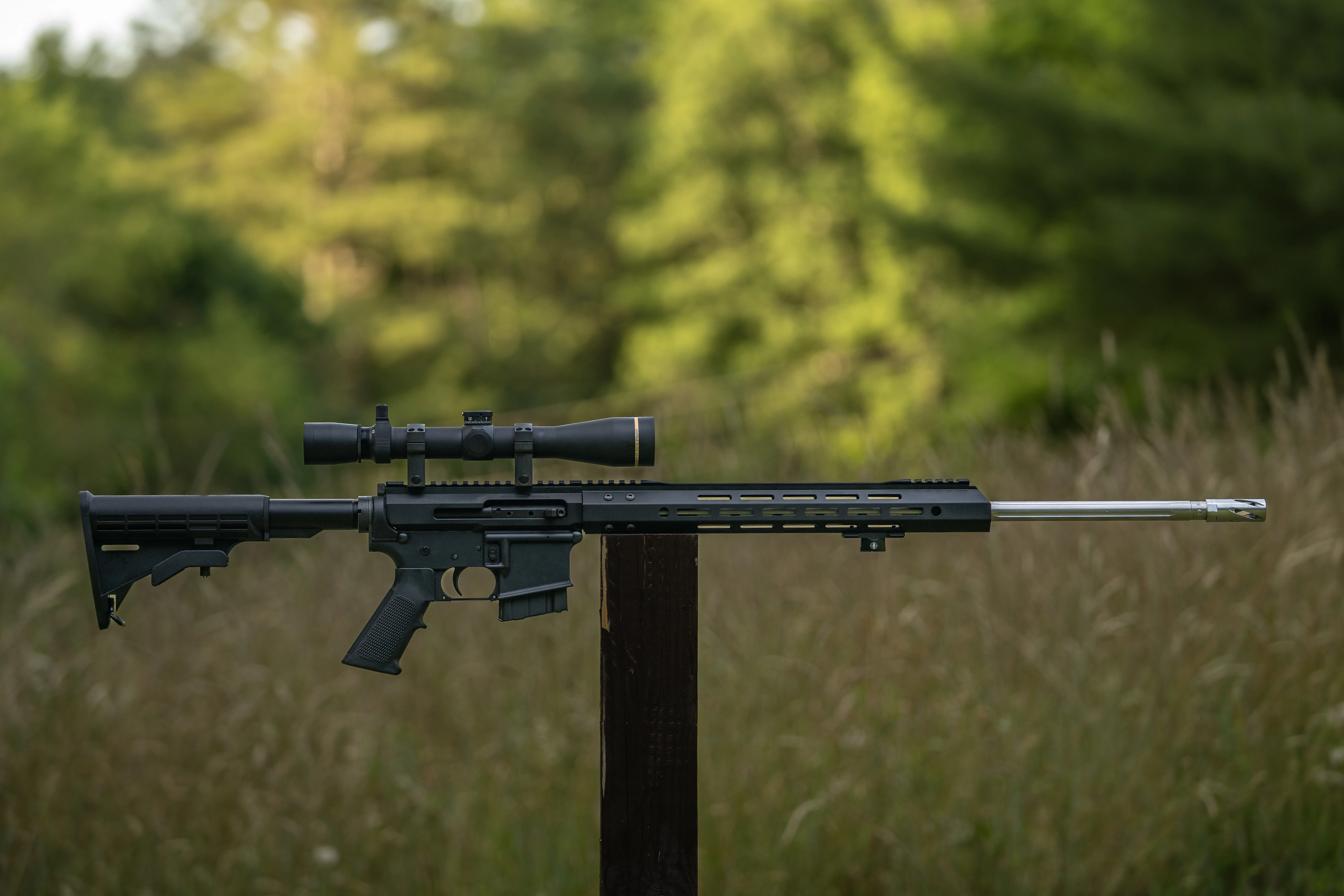 Bear Creek Arsenal BC15 rifle balanced on a post in a field with woods in background. 