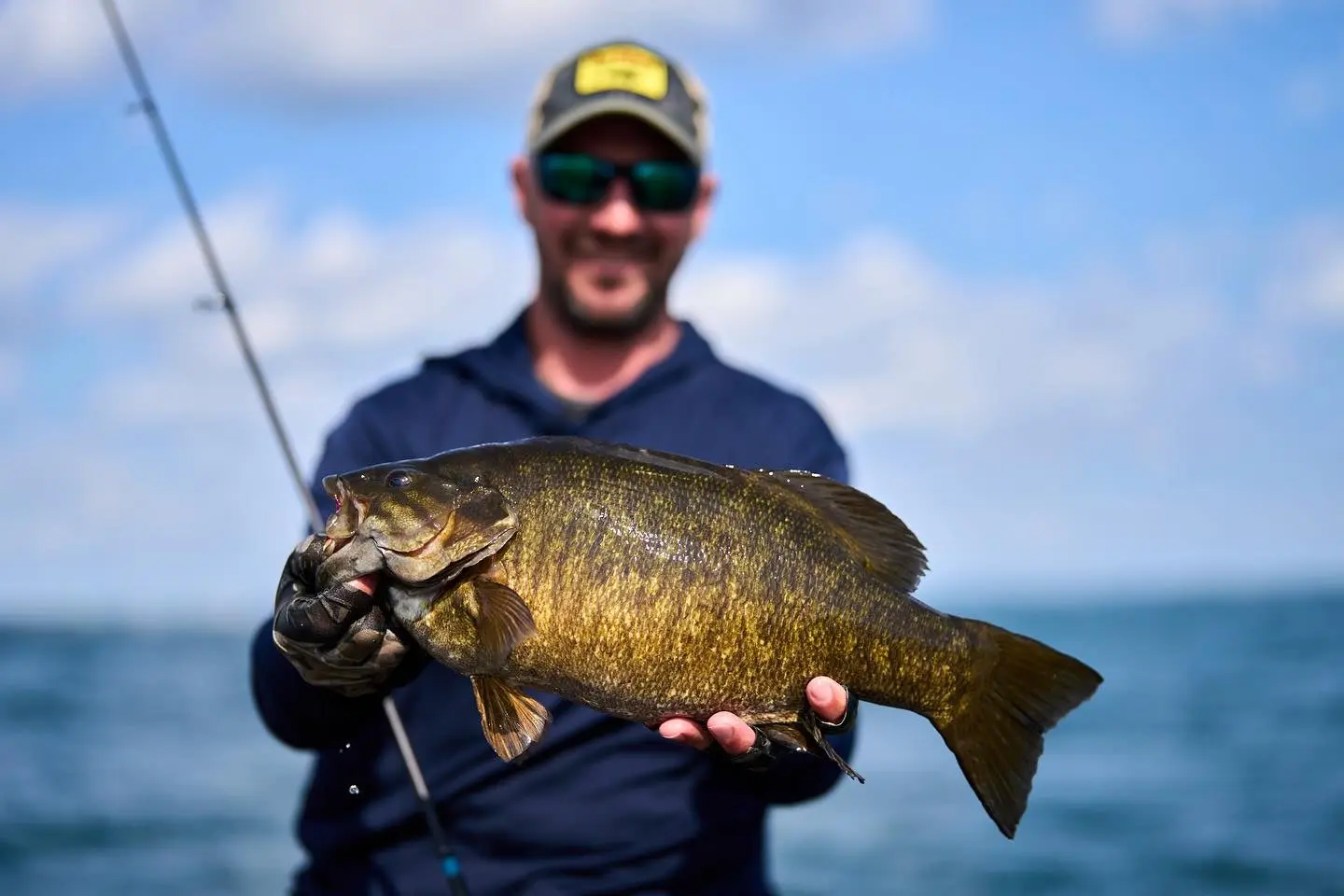 An angler hold up a big smallmouth bass with a lake in the background. 