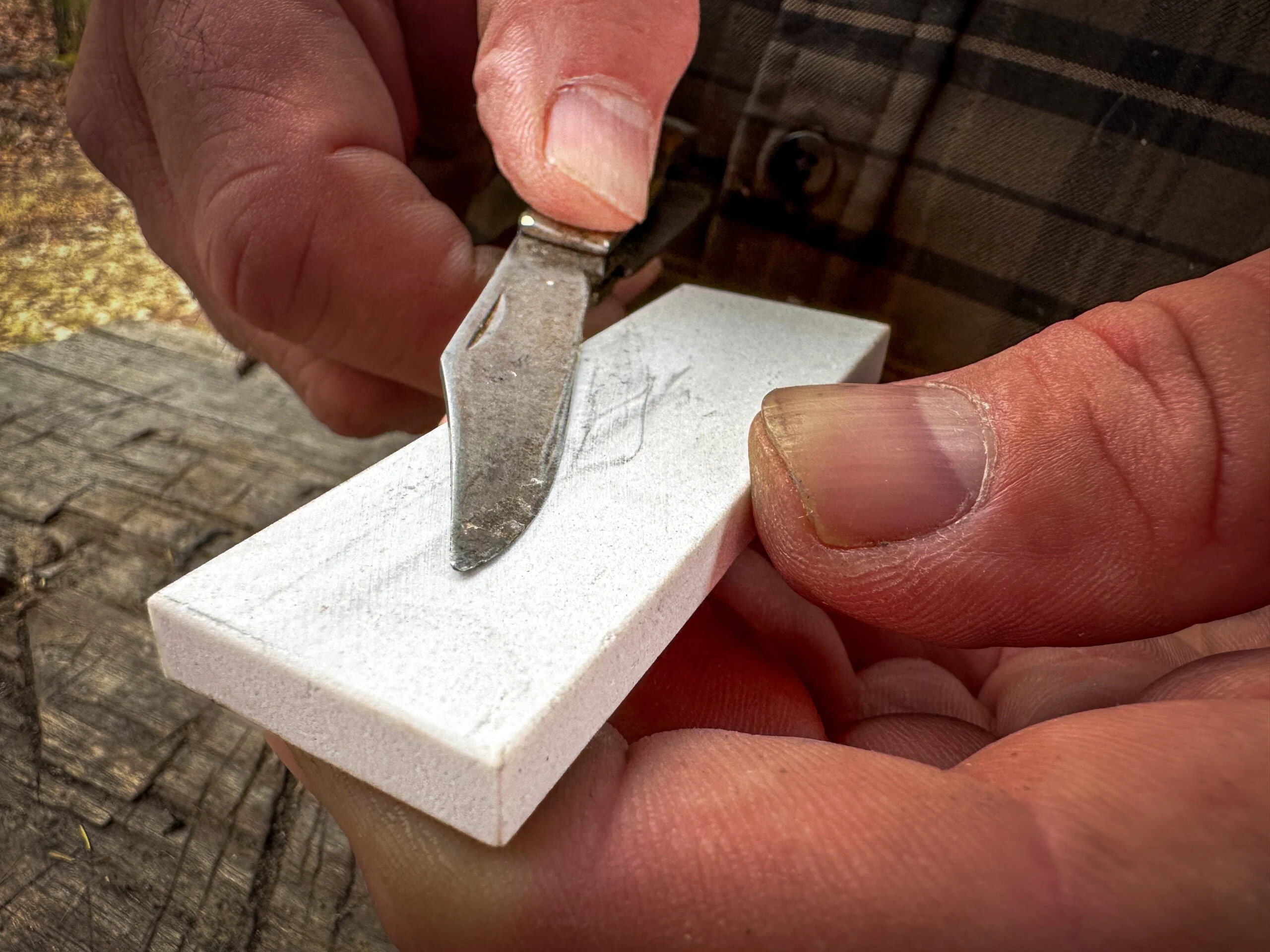 Hands run a pocket knife against a fine-grain whetstone to sharpen it.