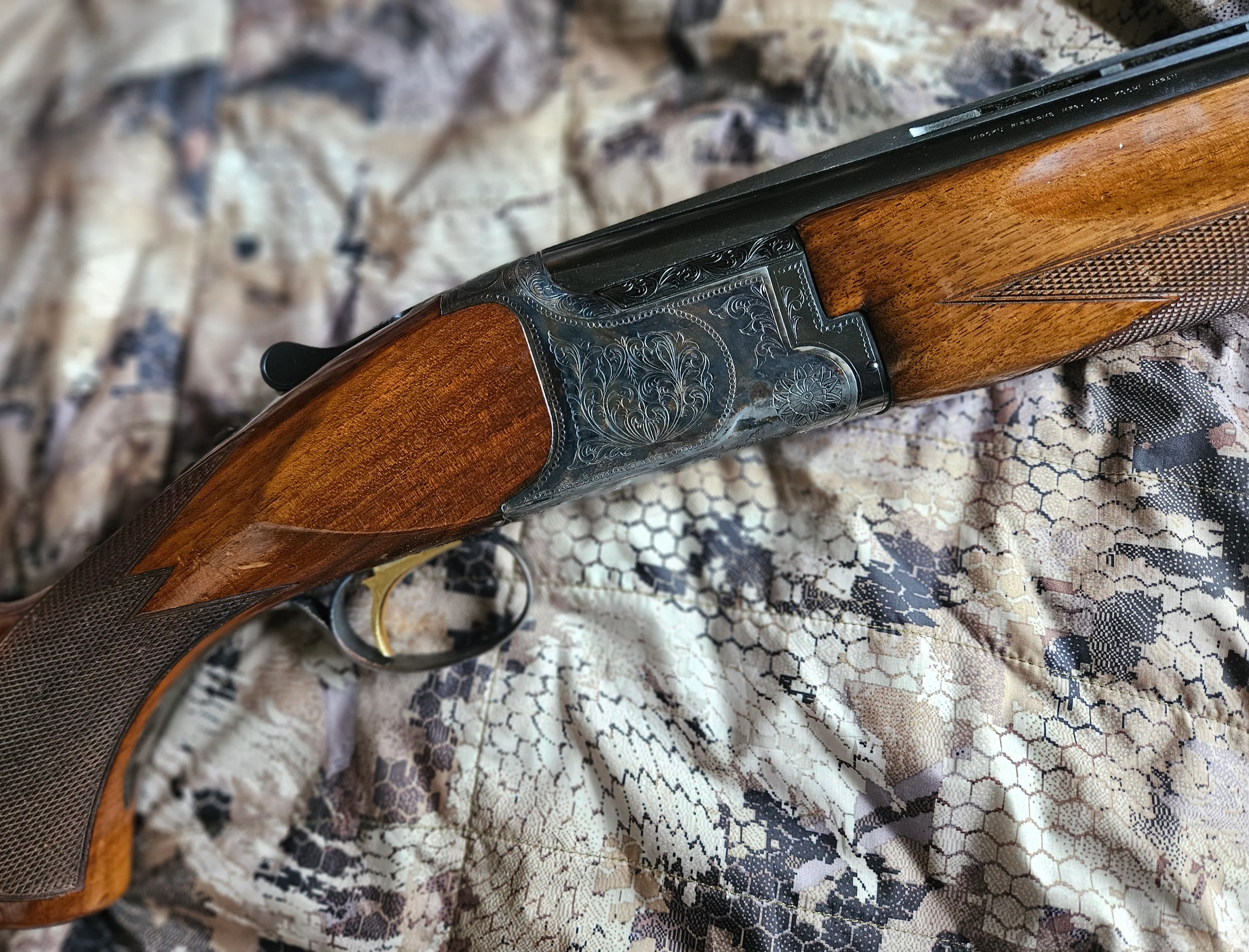 A Charles Daly Miroku Superior Grade over-under shotgun on a camouflage jacket. 