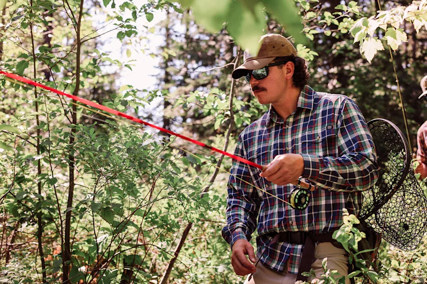 fly angler wearing a plaid shirt walk to a fishing spot