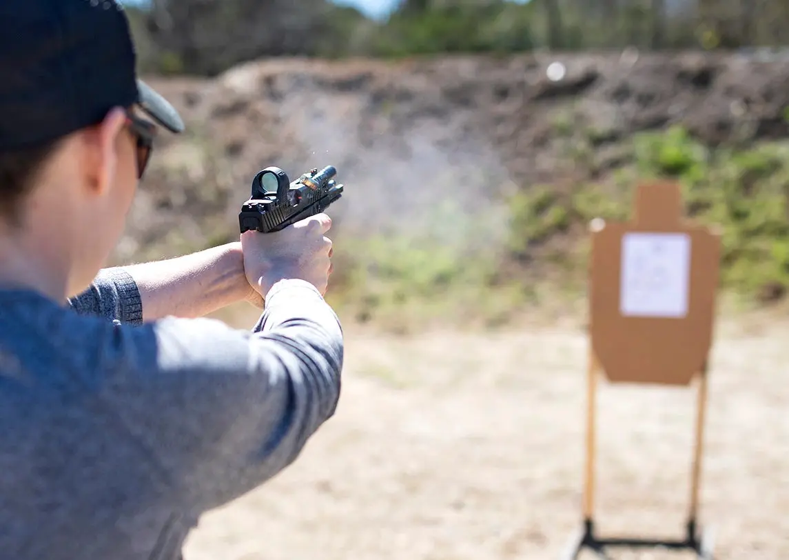 A person on a shooting range firing a pistol with an SRO red-dot sight.