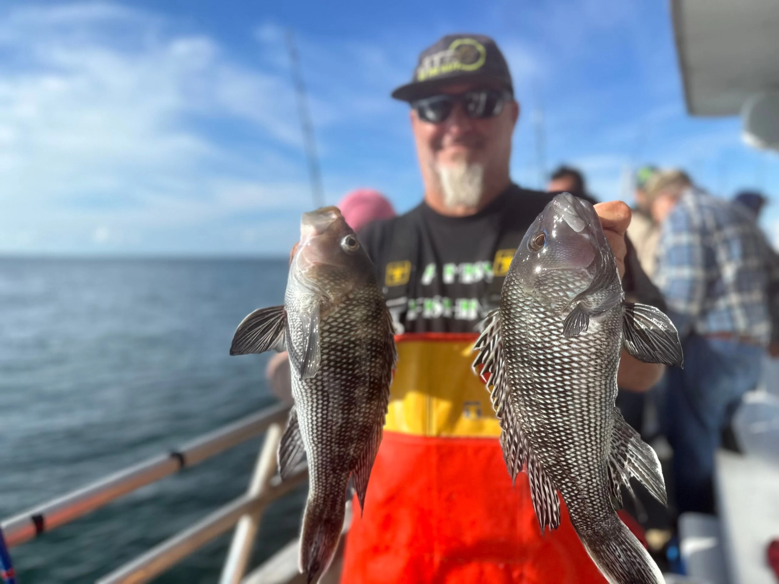 A fisherman on a party boat holds two fish.