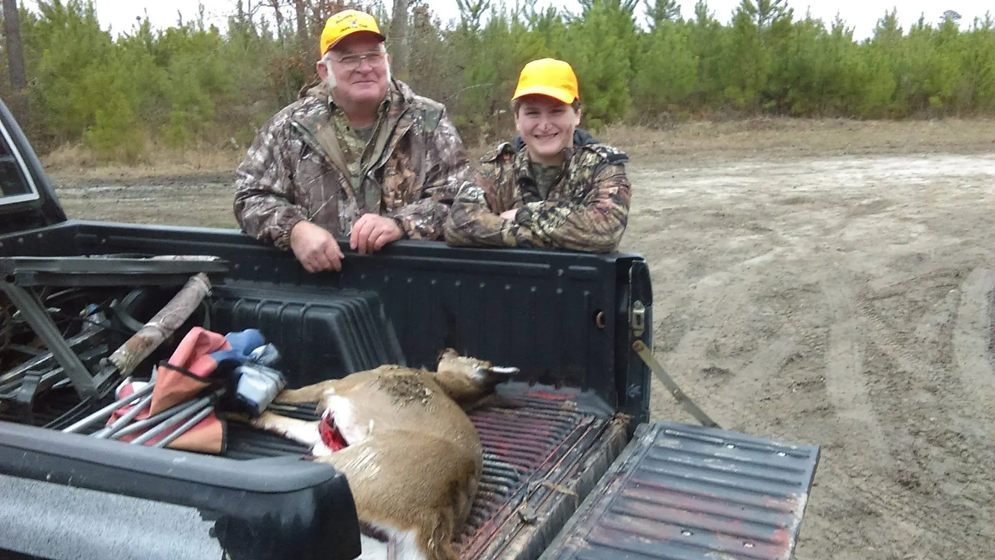 two hunters smile while standing at the side of a pickup truck