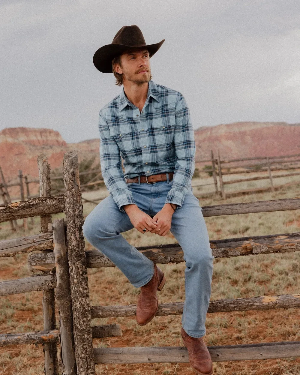 Cowboy wearing Tecovas boots sitting on fence