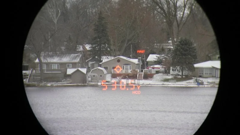 The view through a Vortex Viper HD 4000 rangefinder of a snowy home on the opposite end of a lake. 