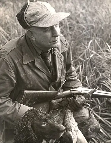 Nash Buckingham sitting in marsh with shotgun and pile of ducks